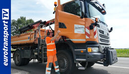 Orange-farbiger Lkw von Straßen NRW in Seitenansicht mit einem vor dem Lkw stehenden Mitarbeiter.